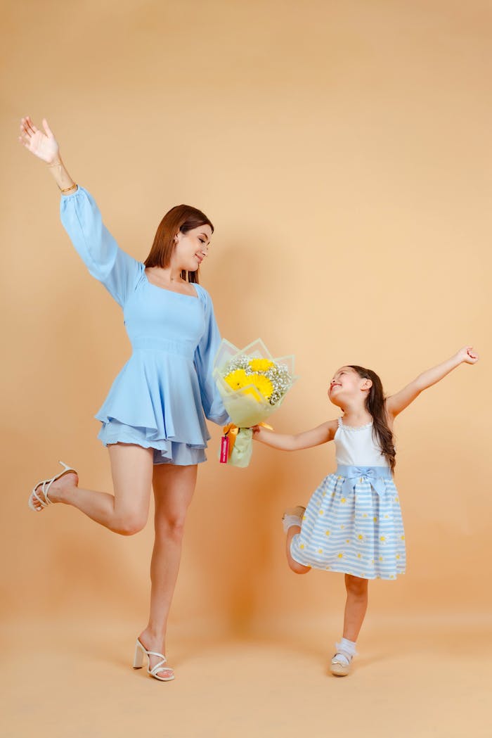 Joyful mother and daughter posing with flowers against a warm studio backdrop.