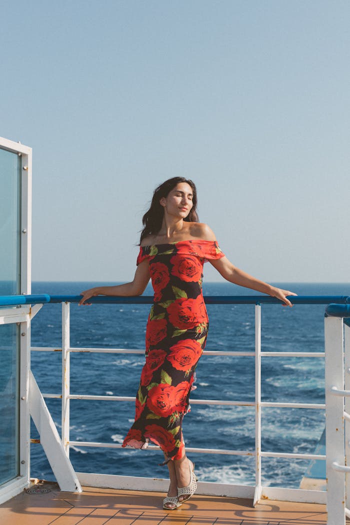 Woman in floral dress enjoying ocean view on a cruise ship under clear blue skies.