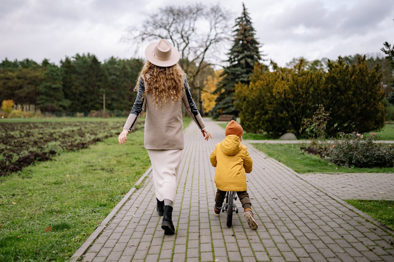 A mother and child enjoy a bicycle ride together in a picturesque autumn park pathway.
