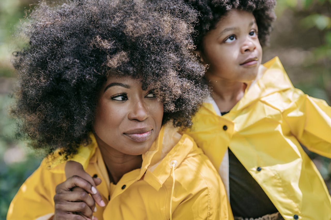 A mother and child share a tender moment outdoors wearing matching yellow raincoats.